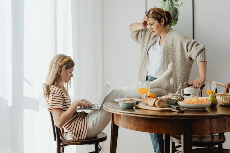 mother feeling annoyed with her daughter with feet on table while using laptop