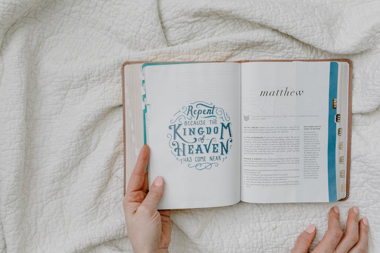 Open Bible with focus on Matthew passage and text 'Repent'. Hands showing, resting on a quilt.